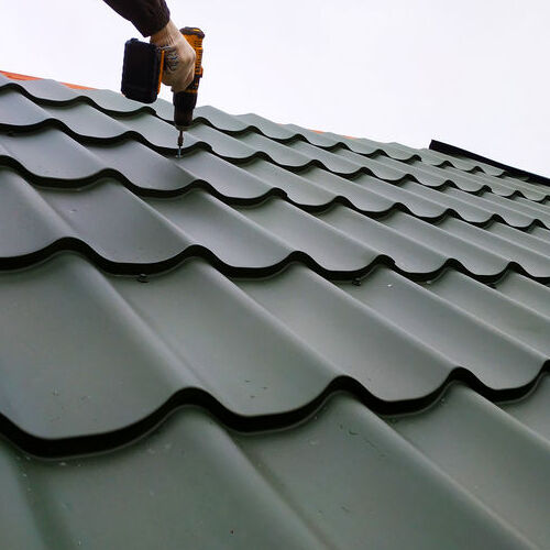 A Roofer Drills in Metal Tile Roofing.