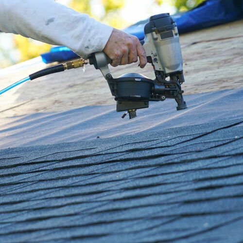 A Roofer Nails in Shingles.